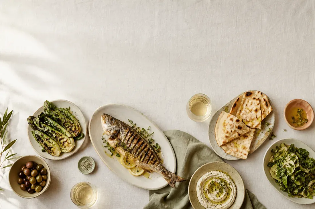 Shared Mediterranean plates on a linen table, seen from above. (AI-generated image)